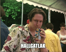 a man in a floral shirt drinking from a juice box with the caption halligatlak on the bottom