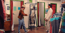 a man in a cowboy hat is shaking hands with a man in a tuxedo in a dressing room .