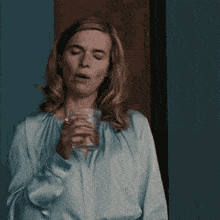 a woman in a blue shirt holds a glass of water