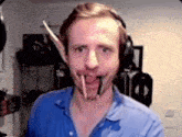 a man with a pencil in his mouth is wearing headphones and a blue shirt .
