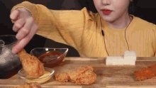 a woman in a yellow sweater is eating fried chicken on a cutting board .
