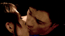 a man in a blue shirt is kissing a woman with a tattoo on his face