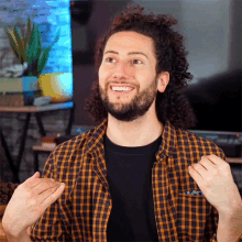 a man with curly hair and a beard wearing a plaid shirt is smiling
