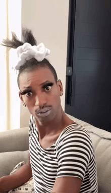 a man wearing a striped shirt and a bow in his hair looks at the camera