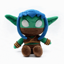 a stuffed elf with blue hair and green ears is sitting on a white surface