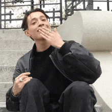 a man wearing a black jacket and a silver ring is smoking a cigarette