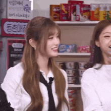 two women are standing next to each other in a store and smiling . one of the women is wearing a tie .