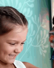 a little girl with braids in her hair is smiling in front of a green wall .