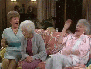 3 of the 4 Golden Girls laughing on a couch together.