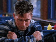 a man in a plaid shirt is hugging his arms and looking down