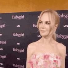 a woman in a pink dress is standing in front of a wall that says babygirl on it .