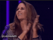 a woman applauds in front of a microphone with the name lialmeida05 on the bottom right