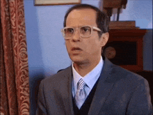 a man wearing glasses and a suit is looking at the camera