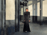 a woman in a long black dress stands in front of a building
