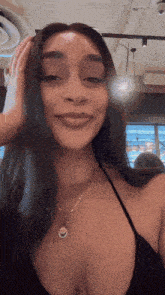 a woman wearing a black top and a gold necklace is smiling and touching her hair .