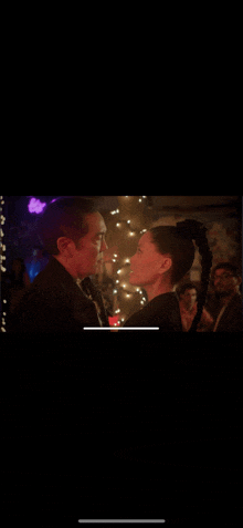 a man and woman are dancing in a dark room with christmas lights behind them