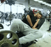 a man sleeping on a bench in a gym with a barbell that says 23 on it