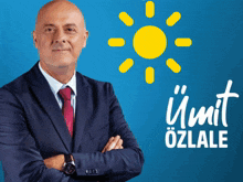 a man in a suit and tie stands with his arms crossed in front of a blue background with umit ozlala written in white