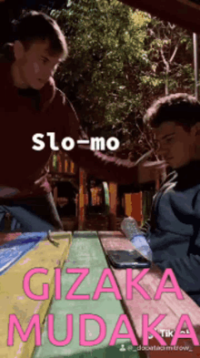 two men sitting at a picnic table with the words slo-mo gizaka mudaka written on the bottom