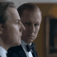 two men in suits and bow ties are standing next to each other in a room .