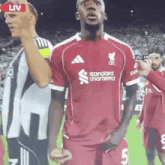 a soccer player wearing a red jersey with the word standard chartered on it is standing on a soccer field .