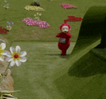 a teletubbies character is walking down a slide in a field of flowers