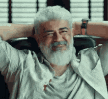 a man with a beard and white hair is sitting in a chair with his hands behind his head and smiling .