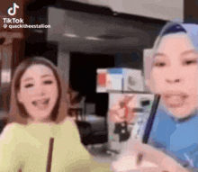 two women are standing next to each other and laughing while looking at a phone .