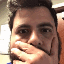 a man with a beard is covering his mouth with his hands .