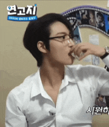 a man wearing glasses and a white shirt is drinking something