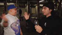 a man wearing a black hoodie with a person on it talks to another man