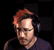 a man with red hair and glasses is wearing headphones and making a funny face .