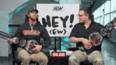 two men are sitting in front of an aew sign