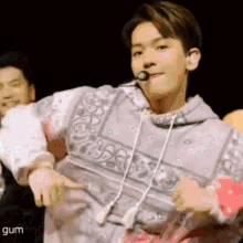 a young man in a bandana hoodie is dancing on a stage with a microphone .