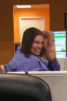 a woman in a blue plaid shirt is smiling and waving her hand