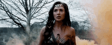 a woman in a wonder woman costume is standing in a field with smoke coming out of her chest .