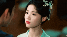 a close up of a woman 's face with a flower in her hair looking at a man