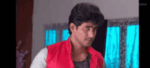 a young man in a red vest is standing in a living room .