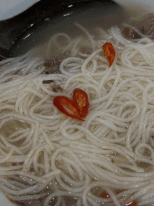 a close up of a bowl of noodles with red peppers on top
