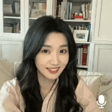 a woman is sitting on a couch in front of a bookshelf and smiling .