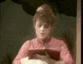 a woman in a pink dress is reading a book while holding a baby .