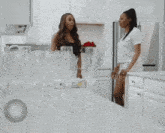 two women are dancing in a kitchen with the words all n on the bottom right