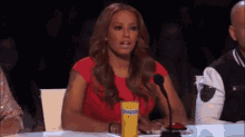 a woman in a red dress is sitting at a table with a microphone and a pineapple drink .