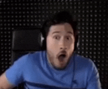 a man wearing headphones is making a surprised face while sitting in front of a computer .