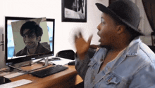 a woman in a hat is sitting in front of a computer screen with a picture of a man on it
