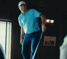 a man in a blue shirt is holding a golf club in a dark room