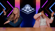 two women are sitting at a table with their hands in the air and dancing .