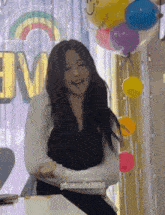 a woman is sitting at a table in front of balloons and laughing .