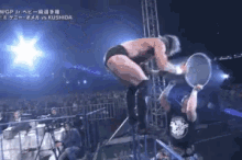 a wrestler is kneeling down holding a ring in front of a crowd while another wrestler stands behind him