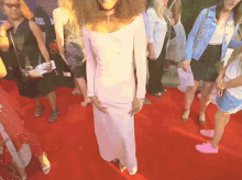 a woman in a white dress stands on a red carpet surrounded by other women